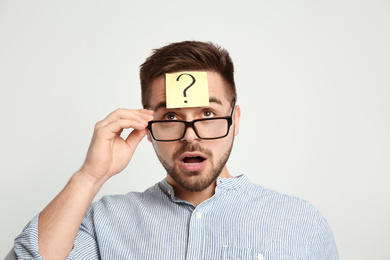 Photo of Emotional man with question mark sticker on forehead against light background