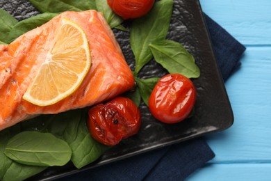 Photo of Tasty grilled salmon with tomatoes, spinach and lemon on light blue table, top view