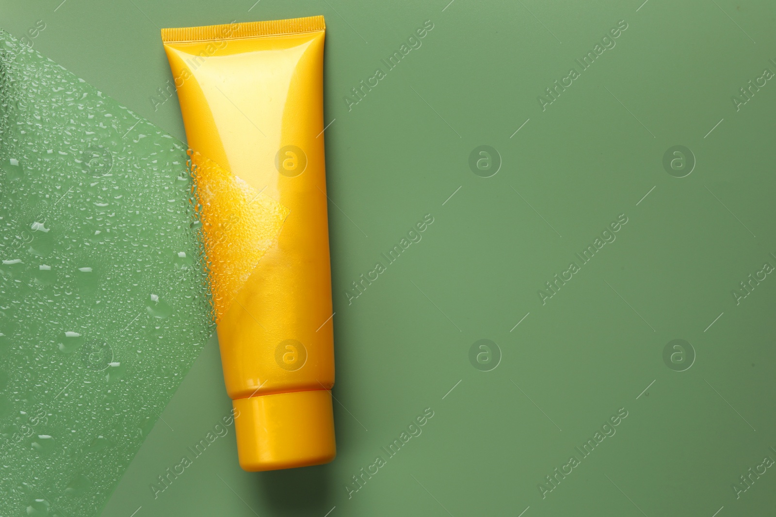 Photo of Tube with moisturizing cream on wet green surface, top view. Space for text