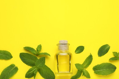 Photo of Bottle of essential oil and mint on yellow background, flat lay. Space for text