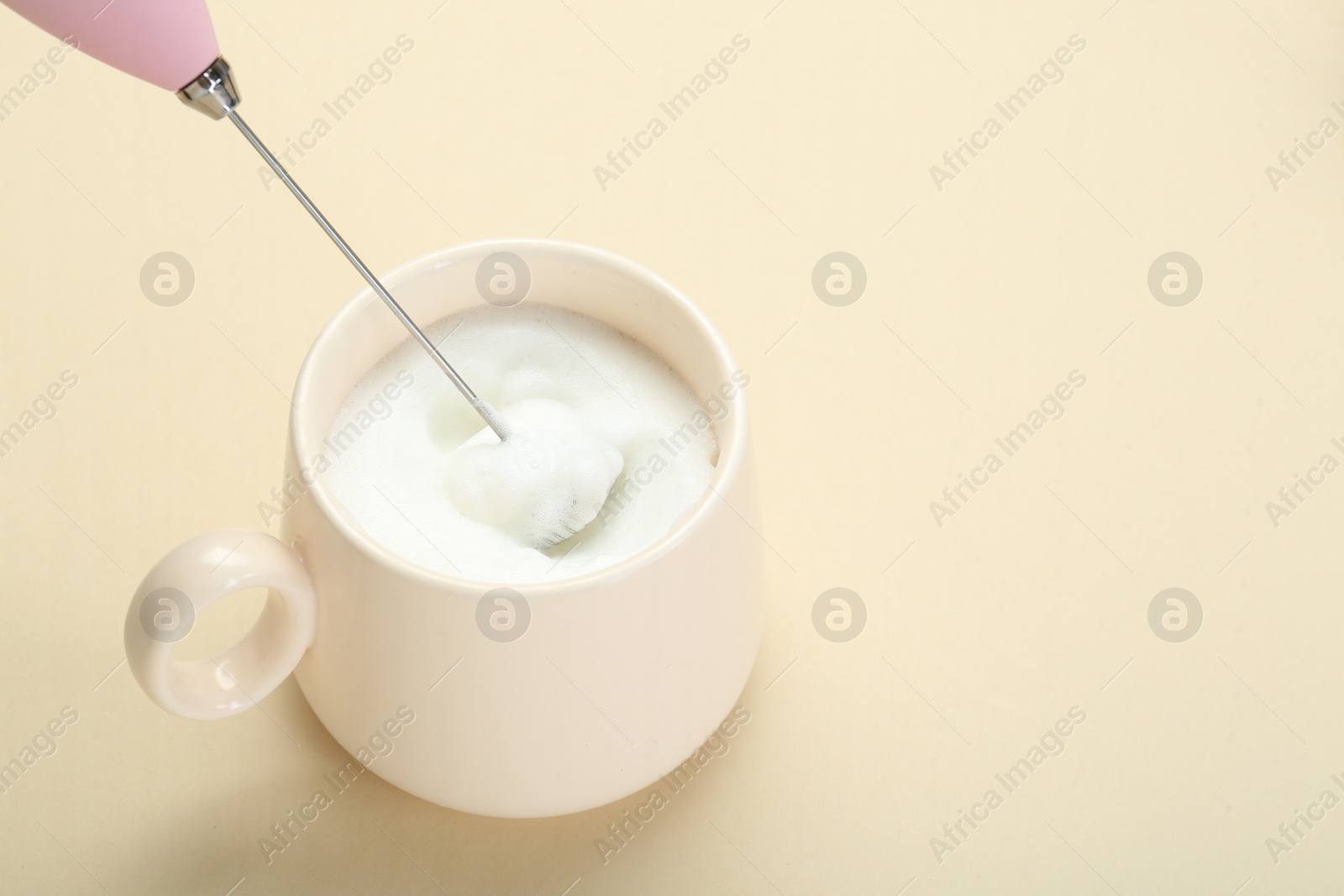 Photo of Whisking milk in cup with mini mixer (milk frother) on beige background. Space for text