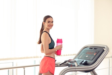Photo of Athletic young woman with protein shake on running machine in gym