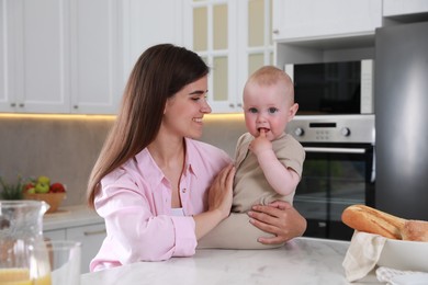 Photo of Happy young woman and her cute little baby spending time together in kitchen