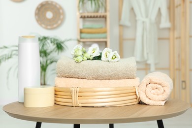 Photo of Soft folded towels, cosmetic products and flowers on wooden table