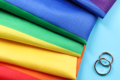 Rainbow LGBT flag and wedding rings on light blue background, top view