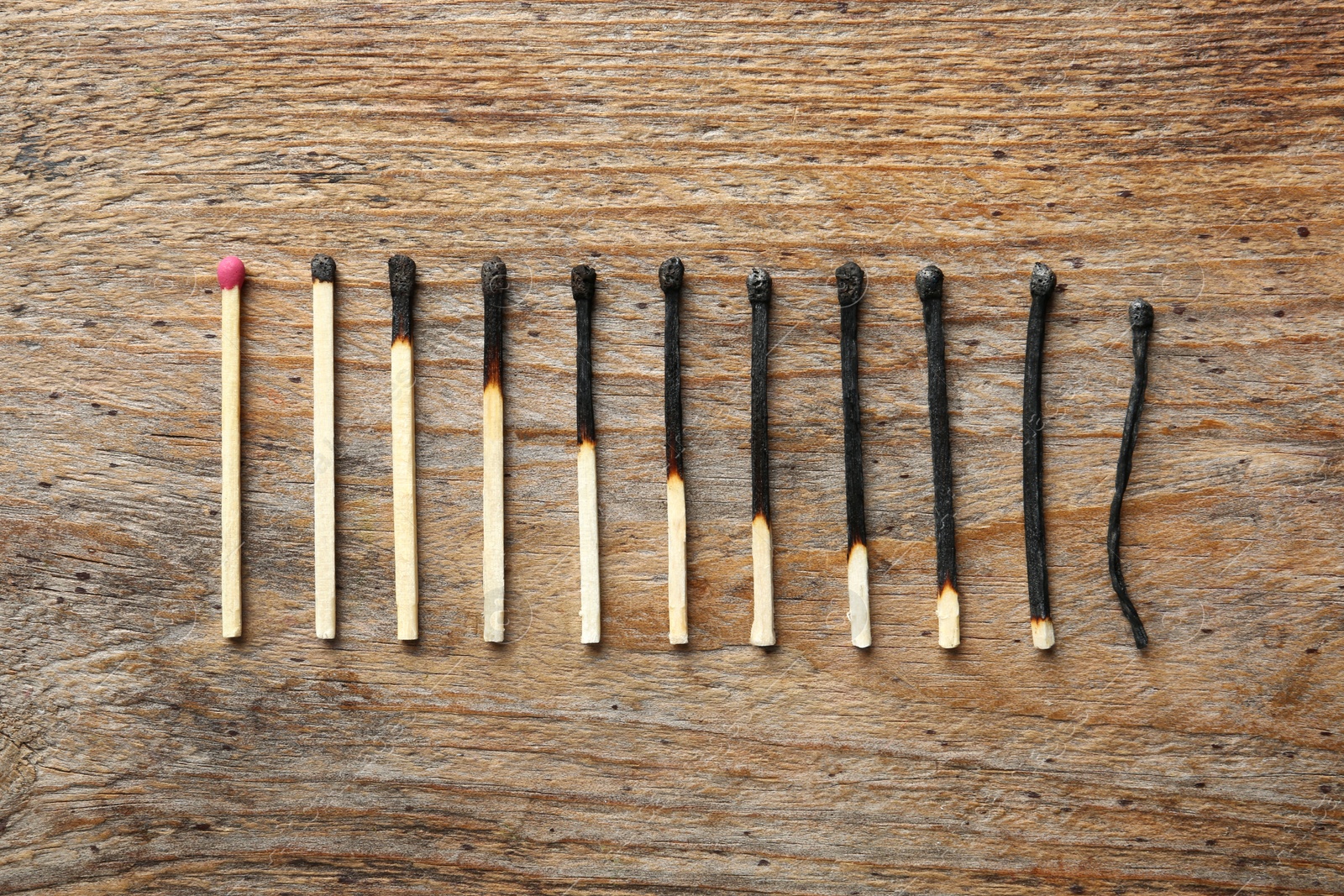 Photo of Row of burnt matches and whole one on wooden background, flat lay. Human life phases concept