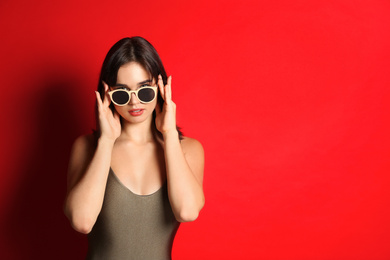 Photo of Beautiful woman in stylish swimsuit and sunglasses on red background. Space for text