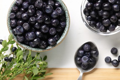 Ripe bilberries and sprigs with leaves on white table, flat lay