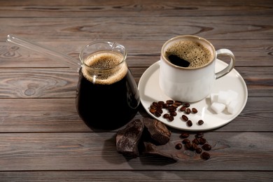 Photo of Glass turkish coffee pot, cup with hot drink, chocolate and beans on wooden table