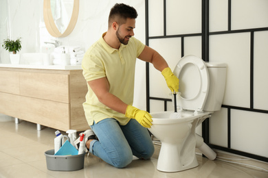 Young man cleaning toilet bowl in bathroom