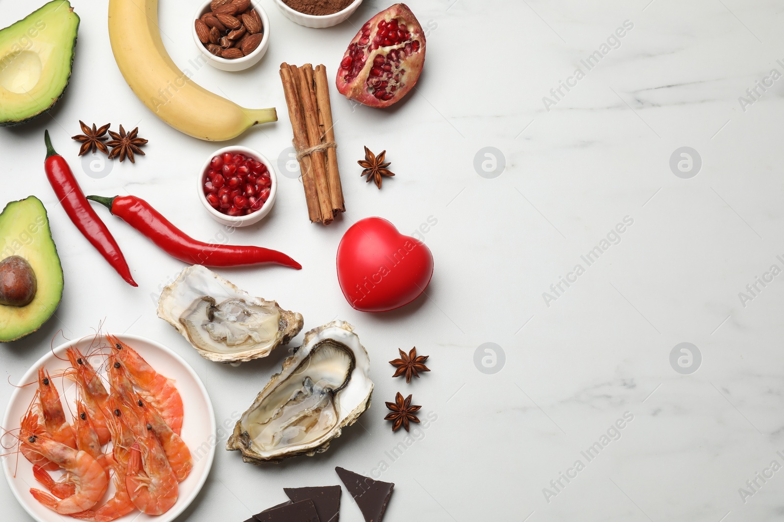 Photo of Natural aphrodisiac. Different food products and red decorative heart on white marble table, flat lay. Space for text