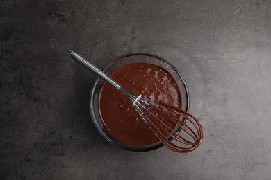 Bowl of chocolate cream and whisk on gray table, top view