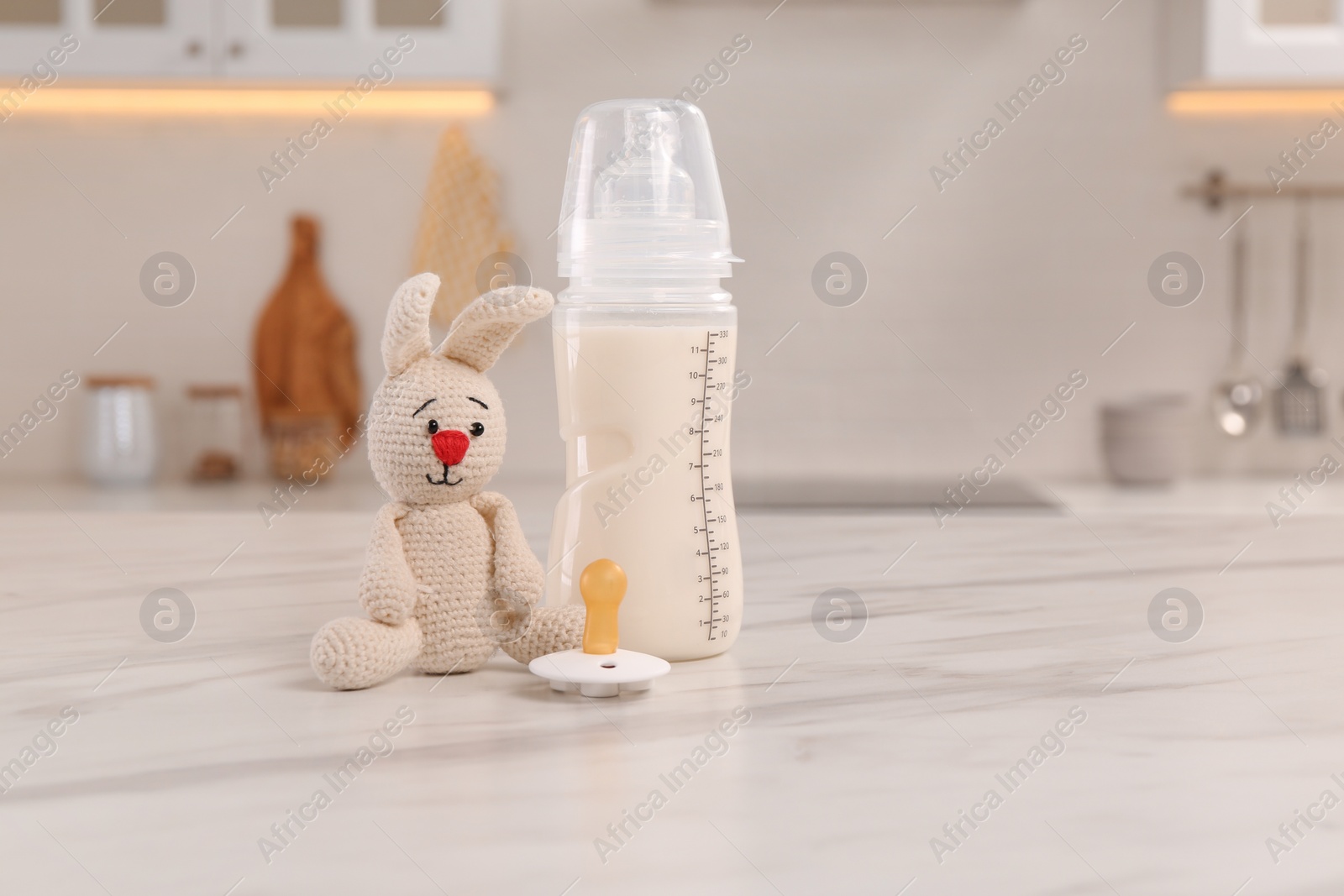 Photo of Baby bottle, toy and pacifier on white marble table indoors, space for text. Maternity leave concept