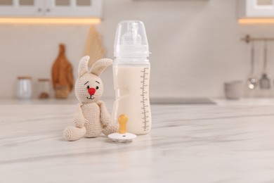 Baby bottle, toy and pacifier on white marble table indoors, space for text. Maternity leave concept