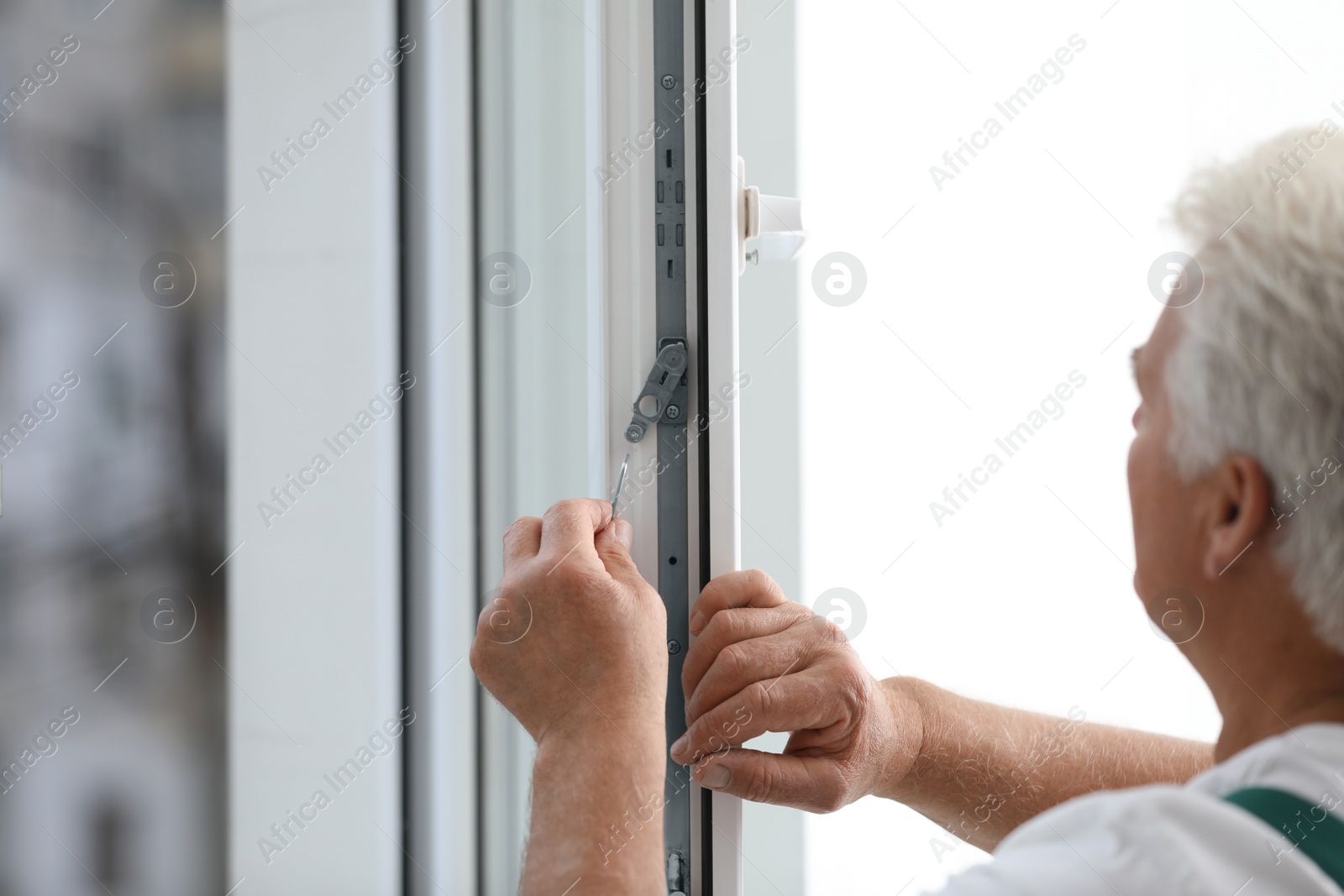 Photo of Mature construction worker repairing plastic window indoors, closeup