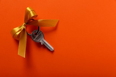Photo of Key with yellow bow on orange background, top view. Space for text. Housewarming party