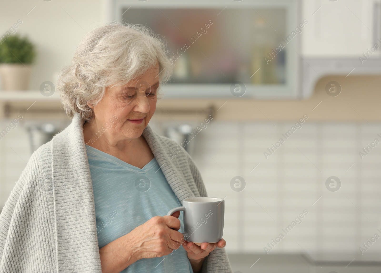 Photo of Elderly woman with cup of tea in kitchen. Space for text