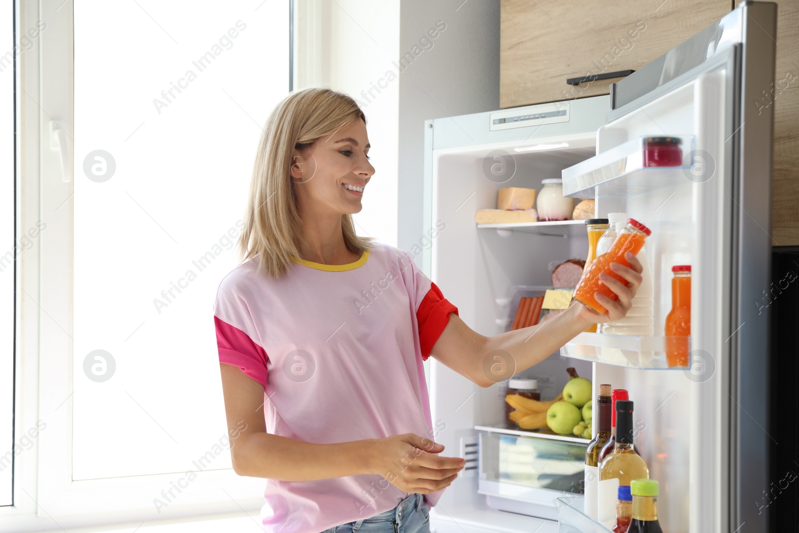 Photo of Woman with bottle of juice near open refrigerator in kitchen