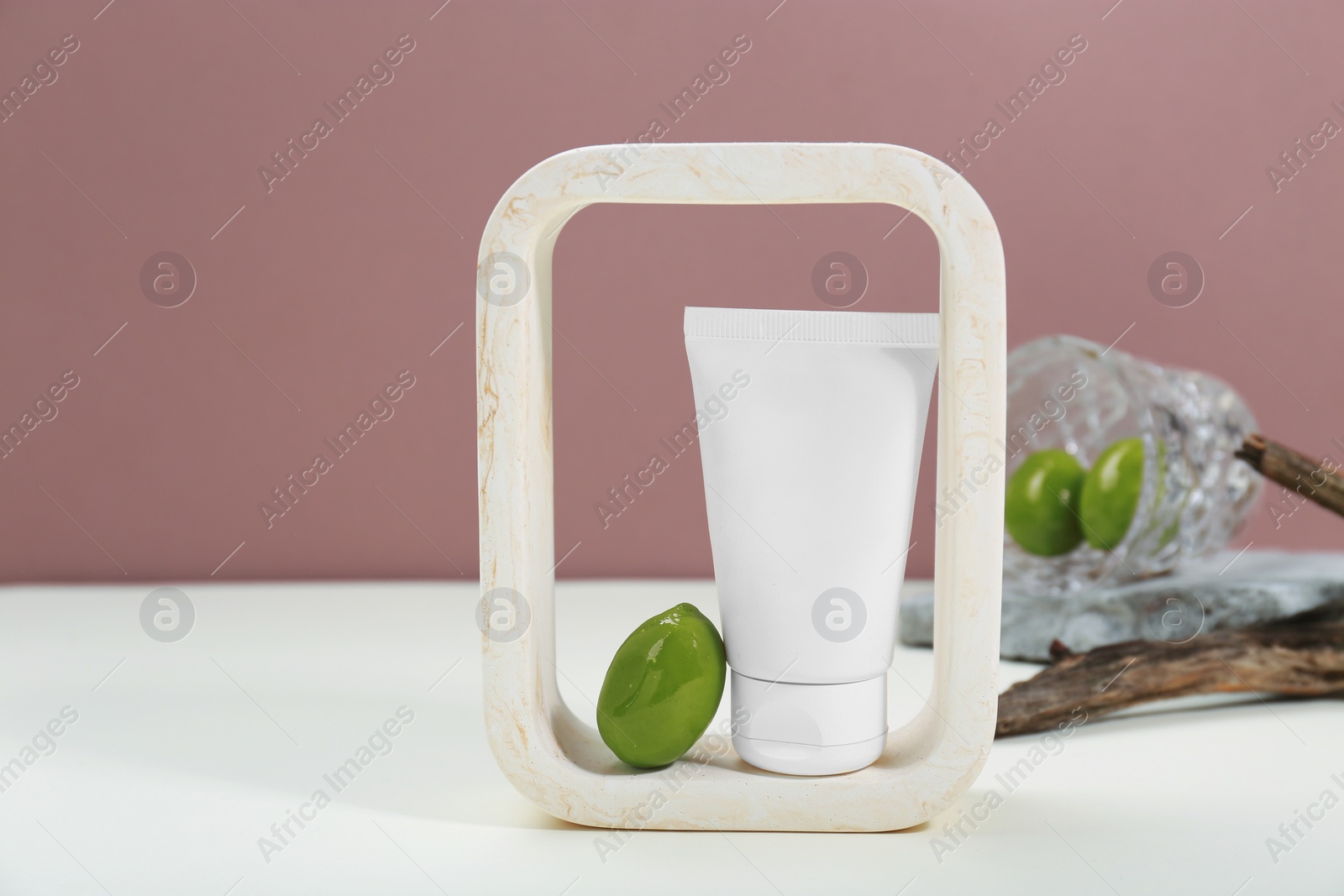 Photo of Tube of cream and olives on white table against pink background, space for text