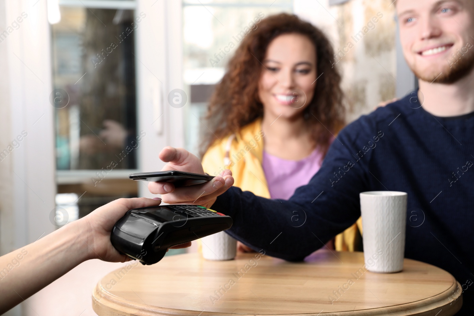 Photo of Clients using smartphone and credit card machine for non cash payment in cafe