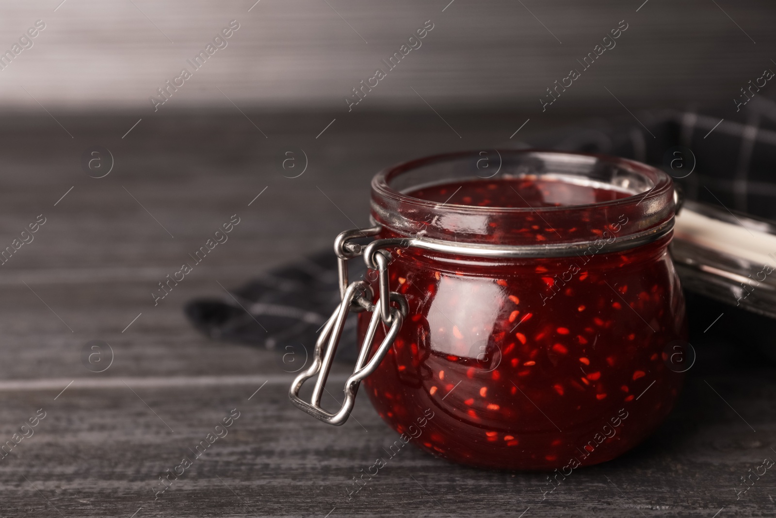 Photo of Homemade delicious raspberry jam on grey wooden table. Space for text