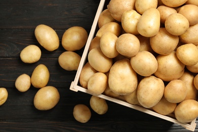 Photo of Raw fresh organic potatoes on black wooden background, top view