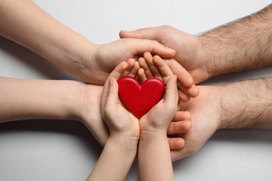 Parents and kid holding red heart in hands on light grey background, top view