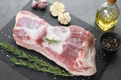 Photo of Piece of raw pork belly, rosemary, spices and garlic on grey table, above view