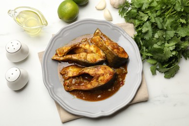 Photo of Tasty fish curry and ingredients on white marble table, flat lay. Indian cuisine