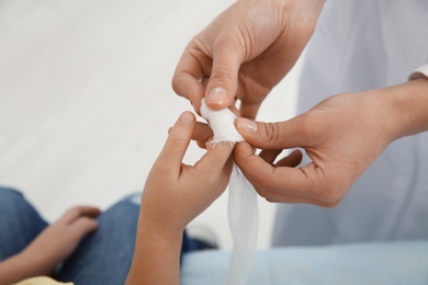 Photo of Female doctor applying bandage on little child's finger in clinic, closeup. First aid