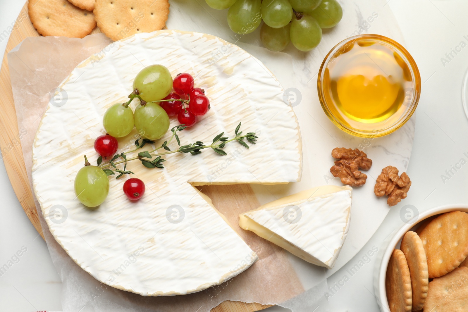 Photo of Brie cheese served with honey, berries and crackers on white table, flat lay