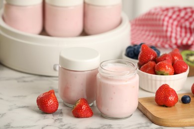 Photo of Modern yogurt maker with full jars and different fruits on white marble table indoors