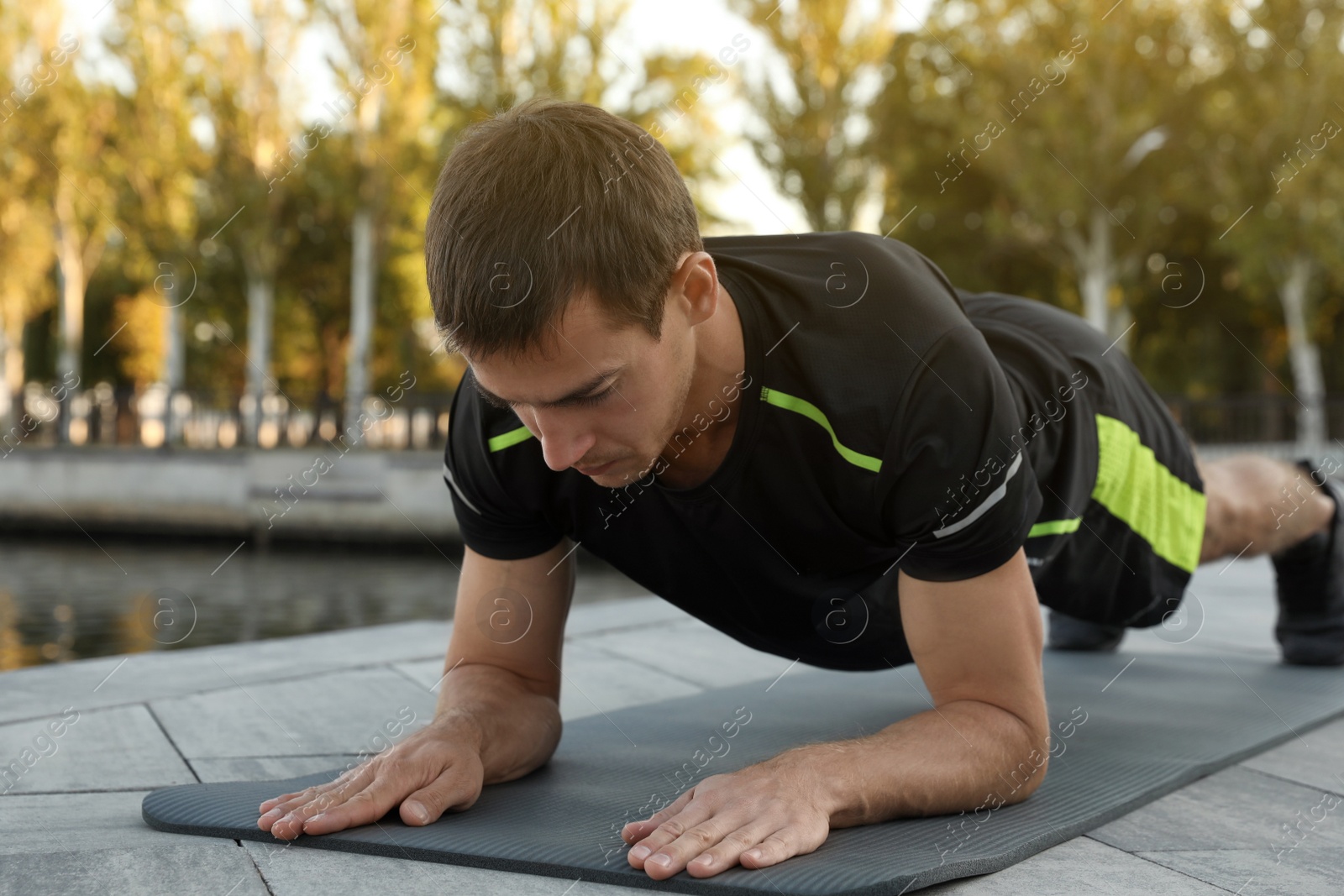 Photo of Sporty man doing plank exercise on mat near river
