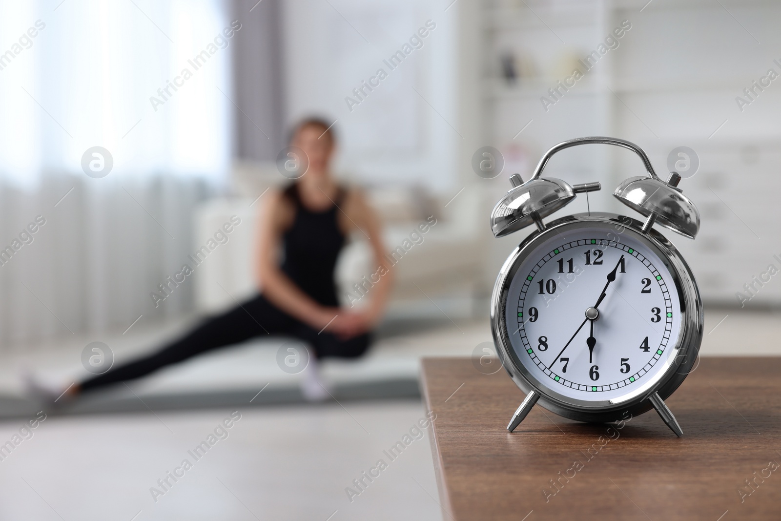 Photo of Morning routine. Alarm clock on wooden table and woman doing exercise, selective focus. Space for text