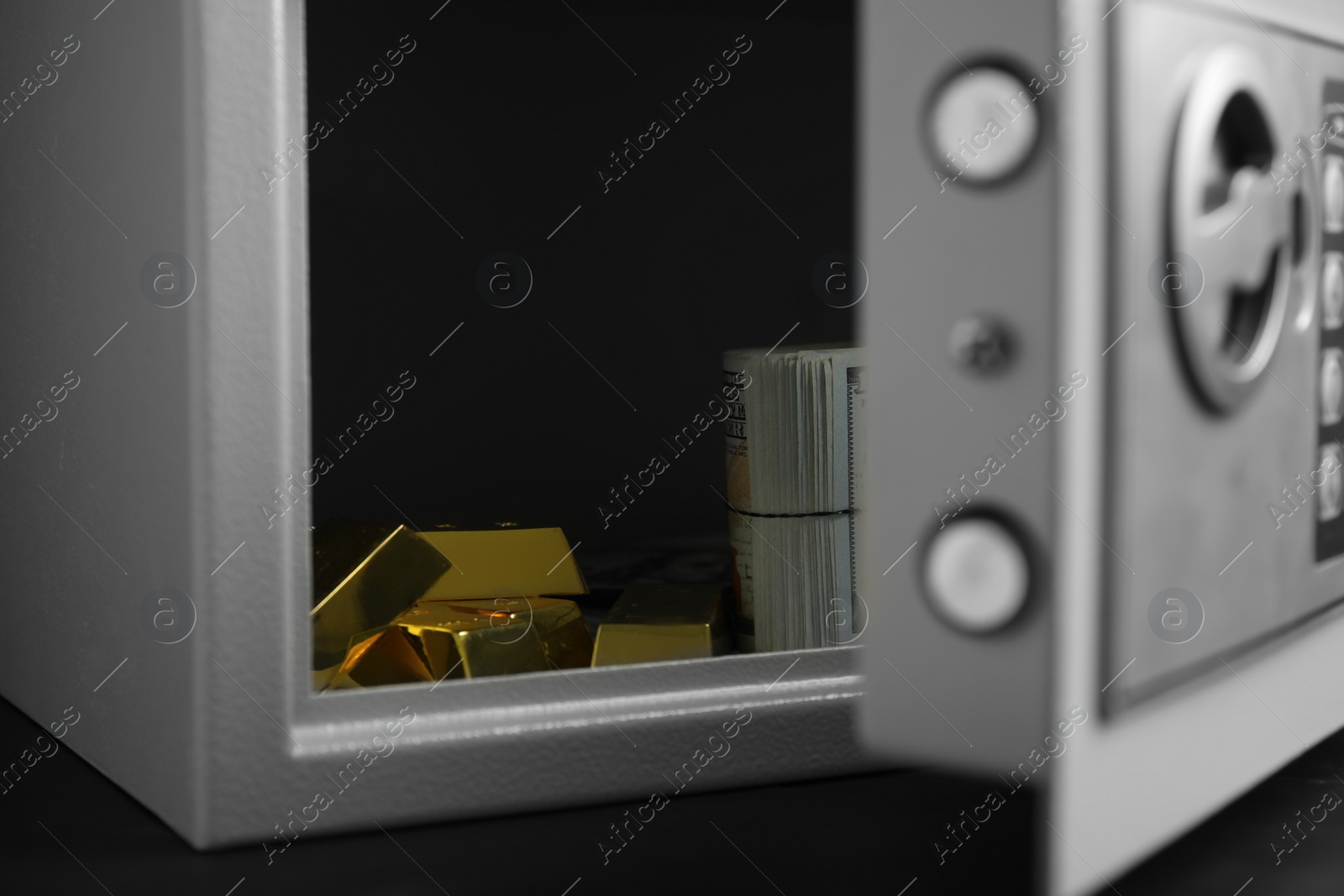 Photo of Open steel safe with money and gold bars on black table, closeup