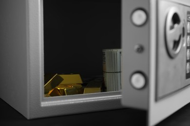 Open steel safe with money and gold bars on black table, closeup