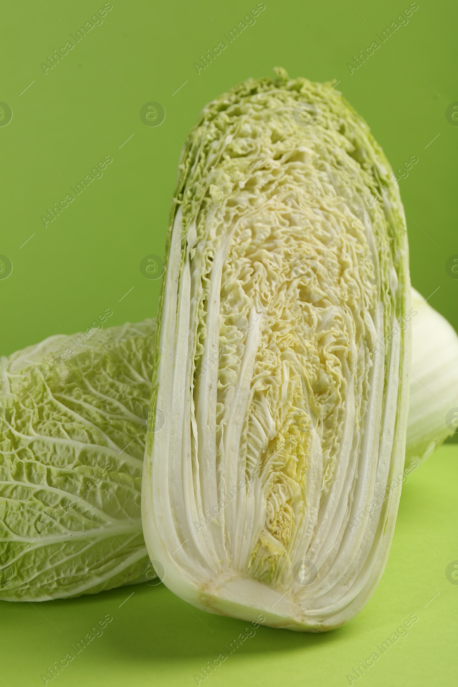 Photo of Whole and cut fresh Chinese cabbage on light green background, closeup