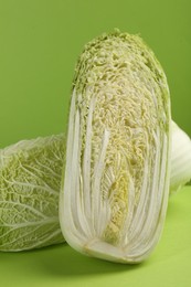 Photo of Whole and cut fresh Chinese cabbage on light green background, closeup