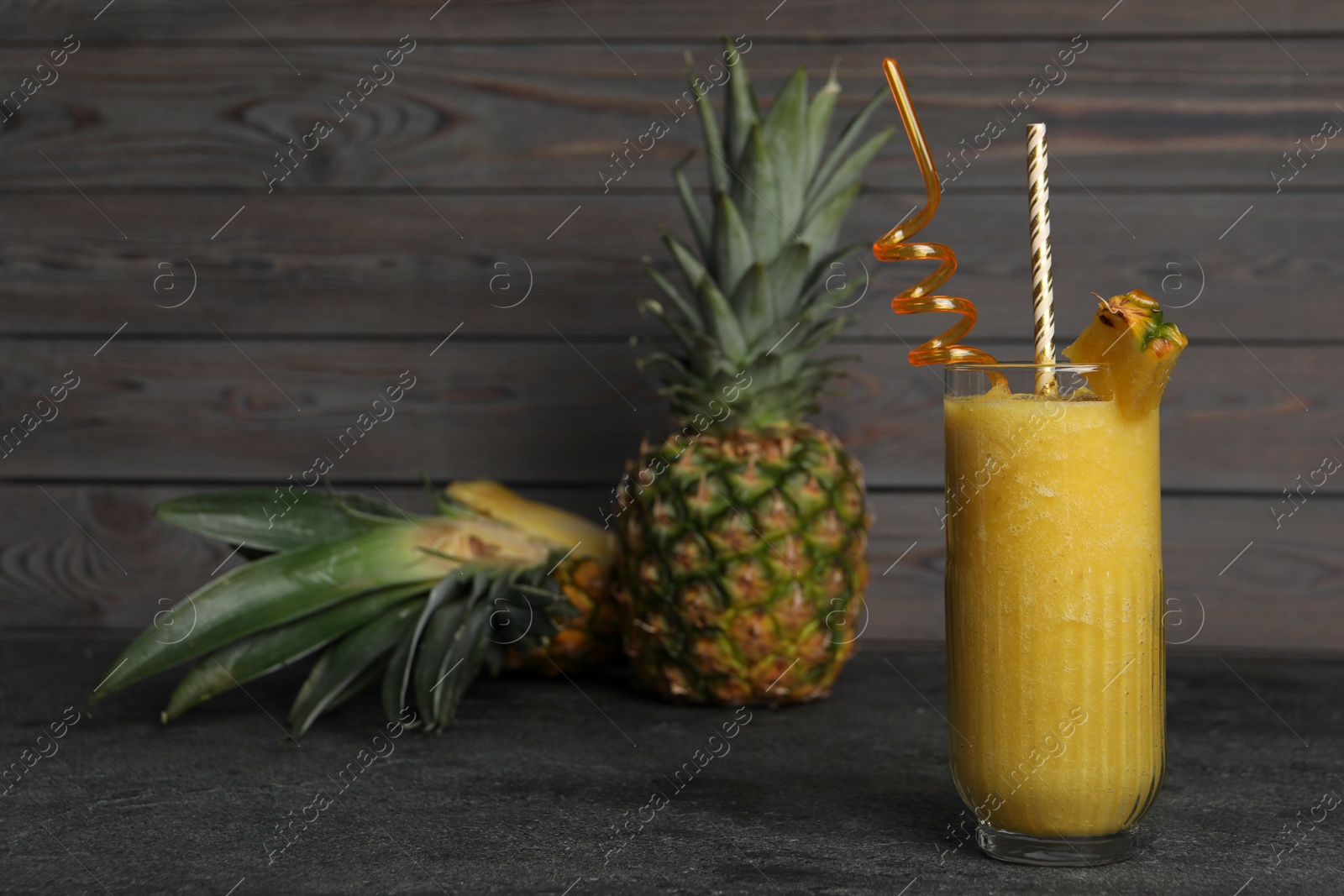 Photo of Tasty pineapple smoothie and fruit on black textured table. Space for text