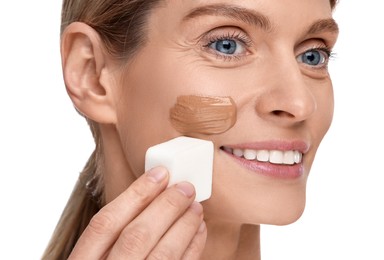 Woman applying foundation on face with makeup sponge against white background