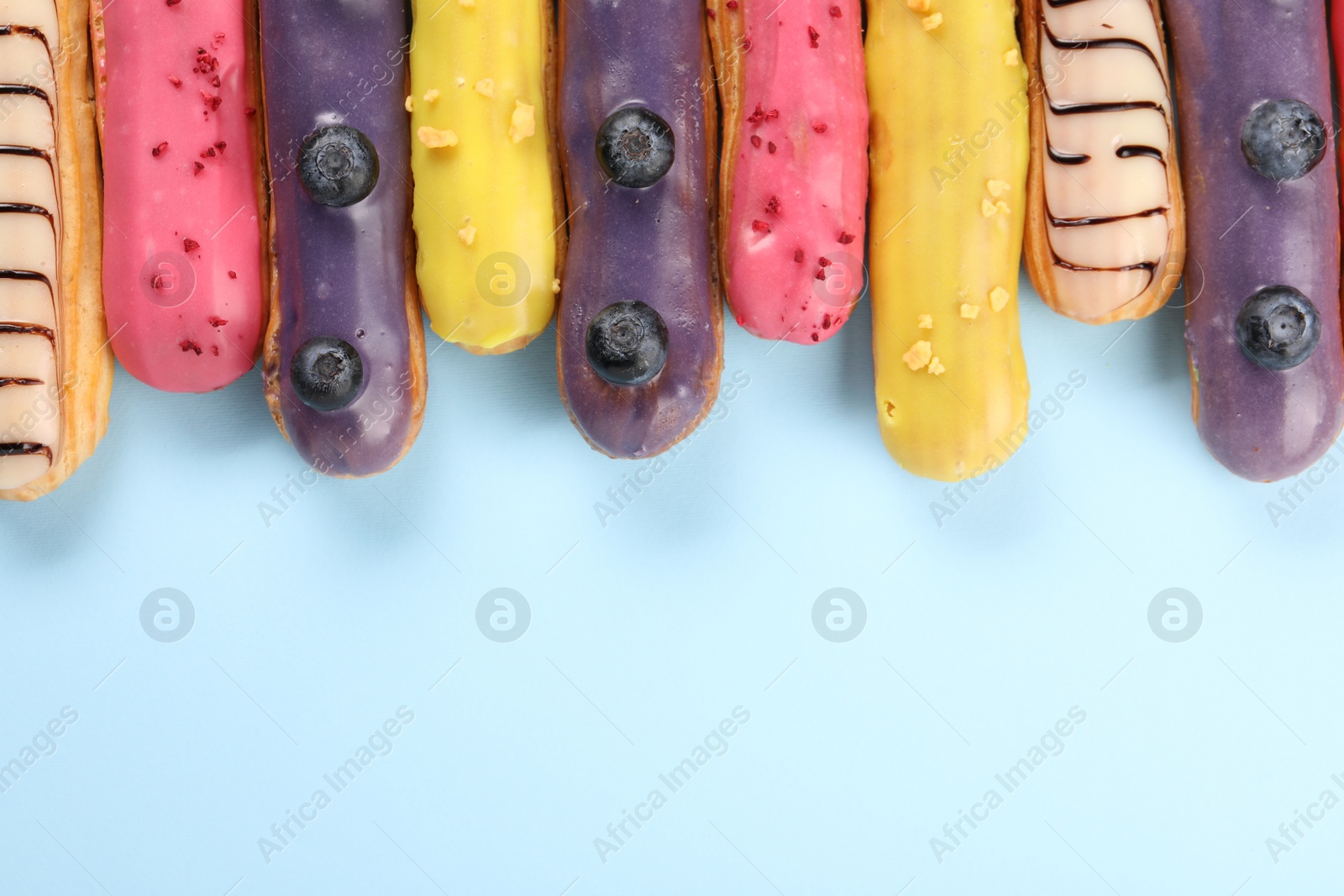 Photo of Delicious eclairs covered with glaze on light blue background, top view. Space for text