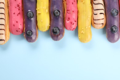 Photo of Delicious eclairs covered with glaze on light blue background, top view. Space for text