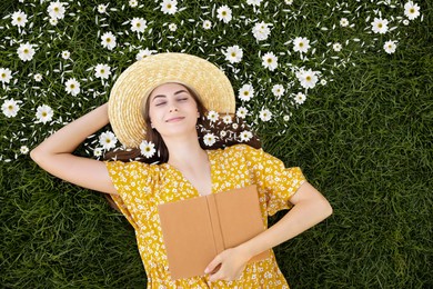 Beautiful young woman with closed eyes lying on green grass, top view. Flowers and petals near her head symbolizing state of mindfulness