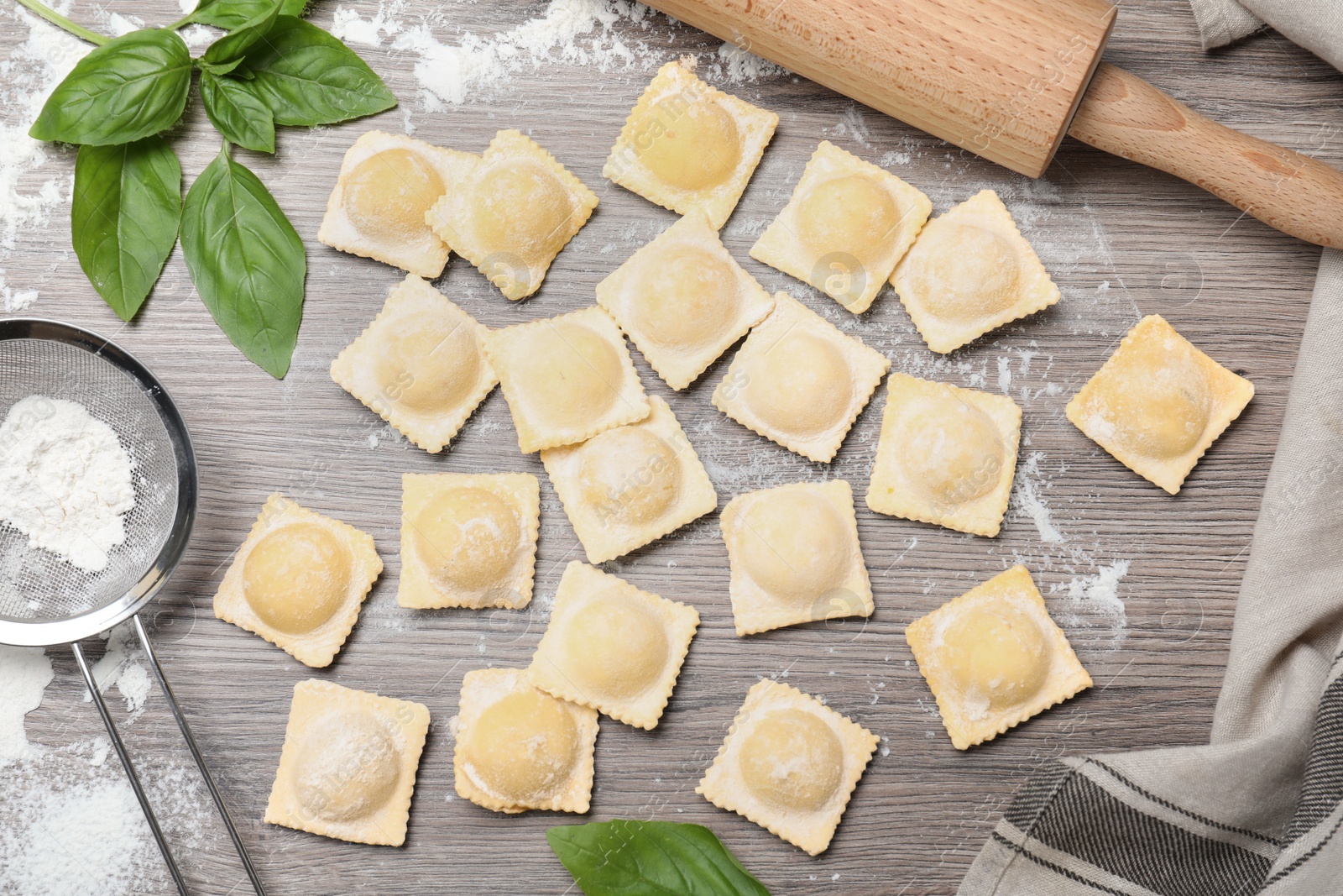 Photo of Uncooked ravioli and basil on wooden table, flat lay