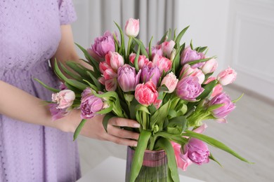 Woman putting bouquet of beautiful tulips in vase indoors, closeup