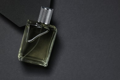 Stylish presentation of luxury men`s perfume in bottle on black background, top view. Space for text