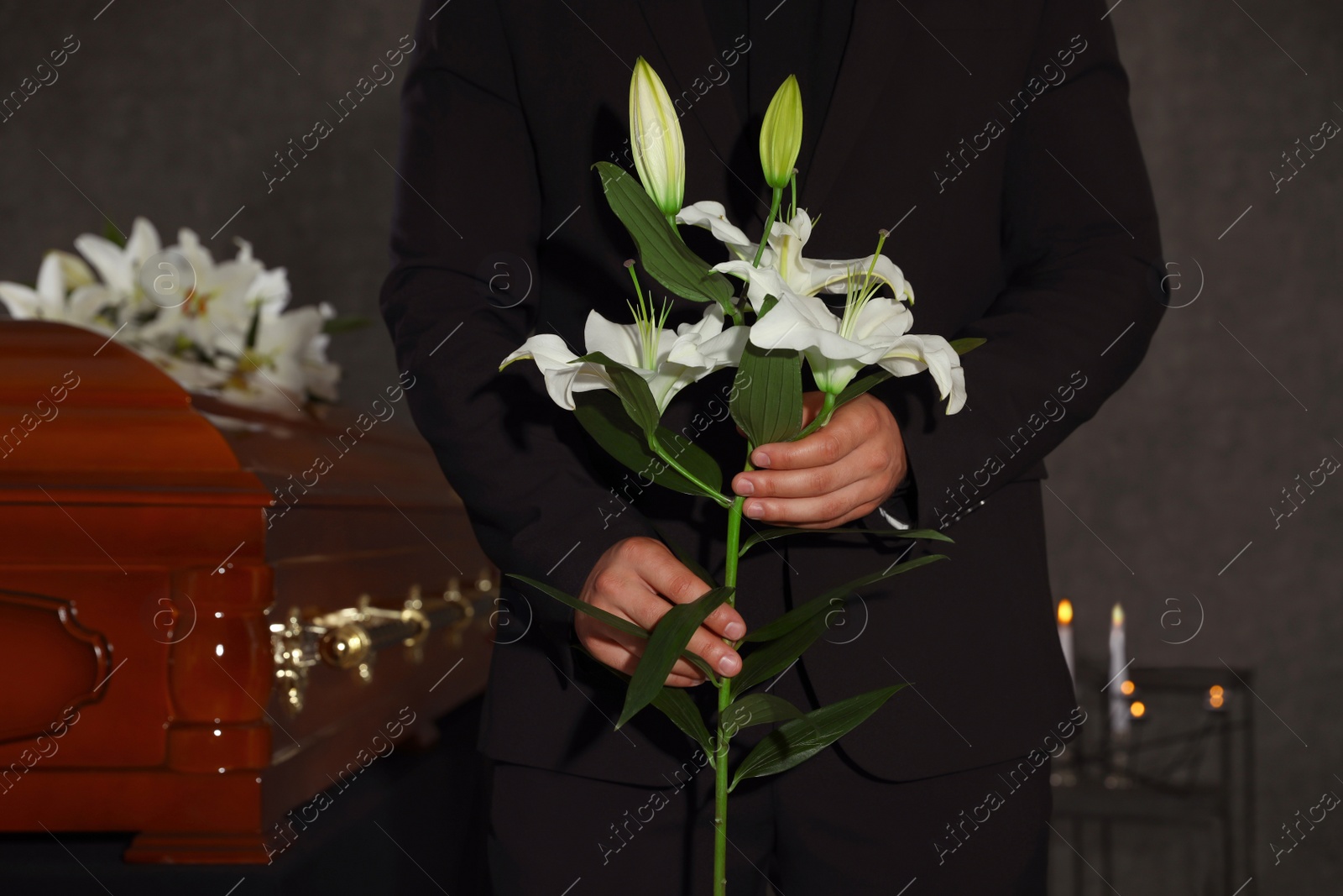 Photo of Young man with white lilies near casket in funeral home, closeup