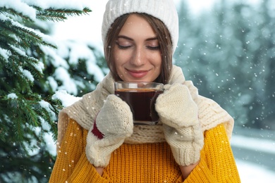 Happy beautiful woman with mulled wine outdoors on snowy day 