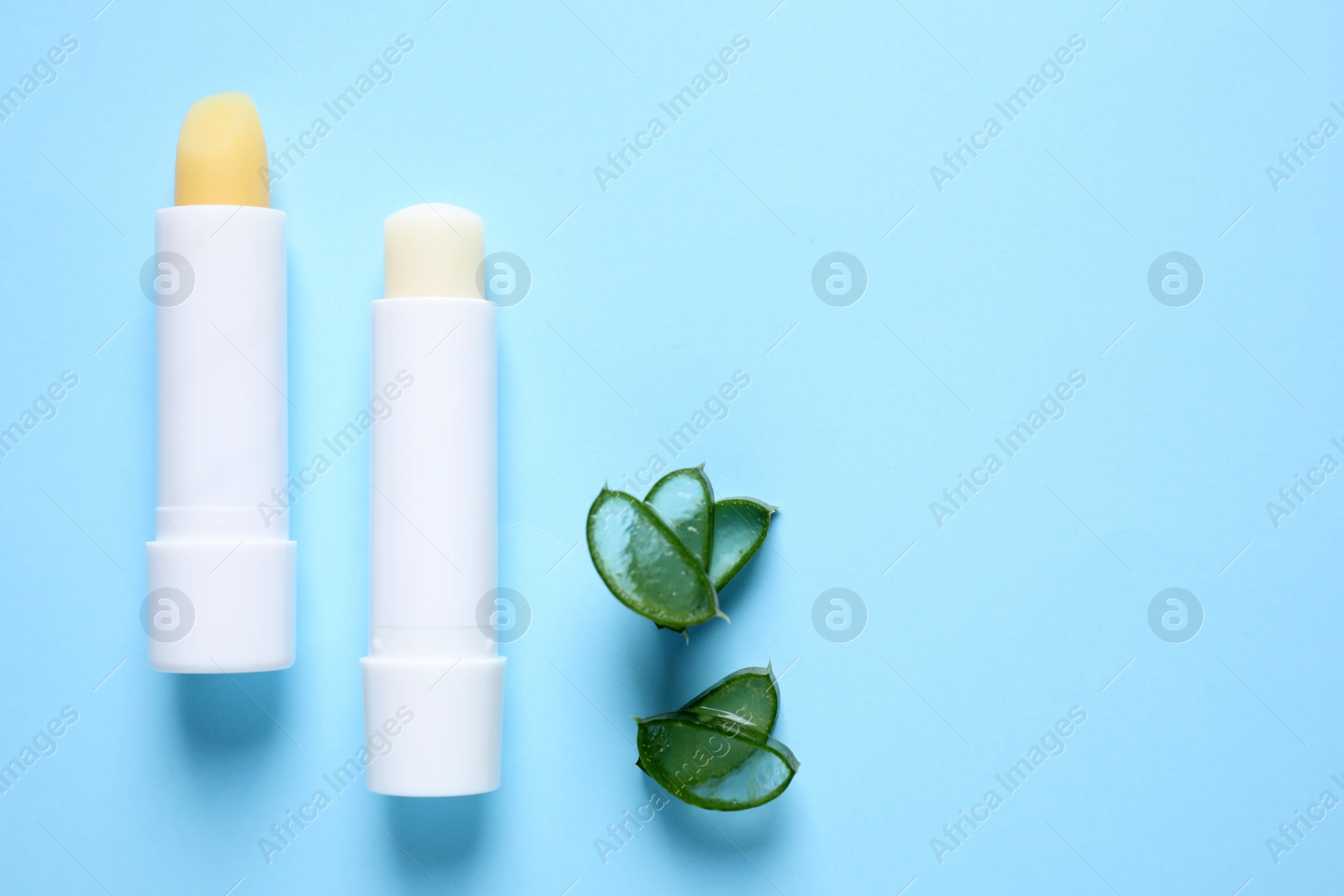 Photo of Hygienic lipsticks and cut aloe vera leaf on light blue background, flat lay. Space for text