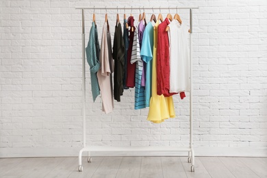 Photo of Wardrobe rack with stylish clothes near brick wall indoors